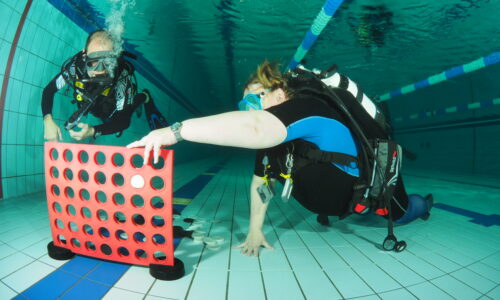 training-taucher-spielt-vier-gewinnt Bild zweier Taucher beim Training, die unter Wasser Vier-Gewinnt spielen.