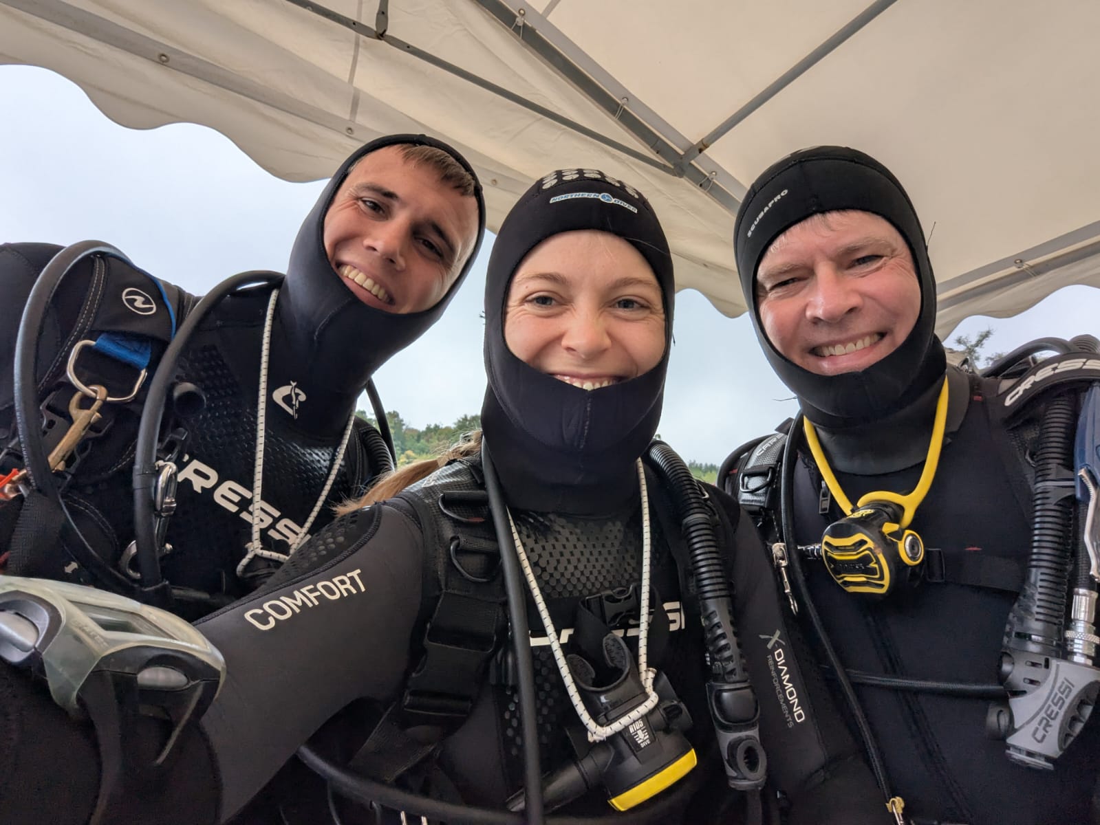 Bild mit drei Tauchern, die in voller Ausrüstung in die Kamera lächeln.