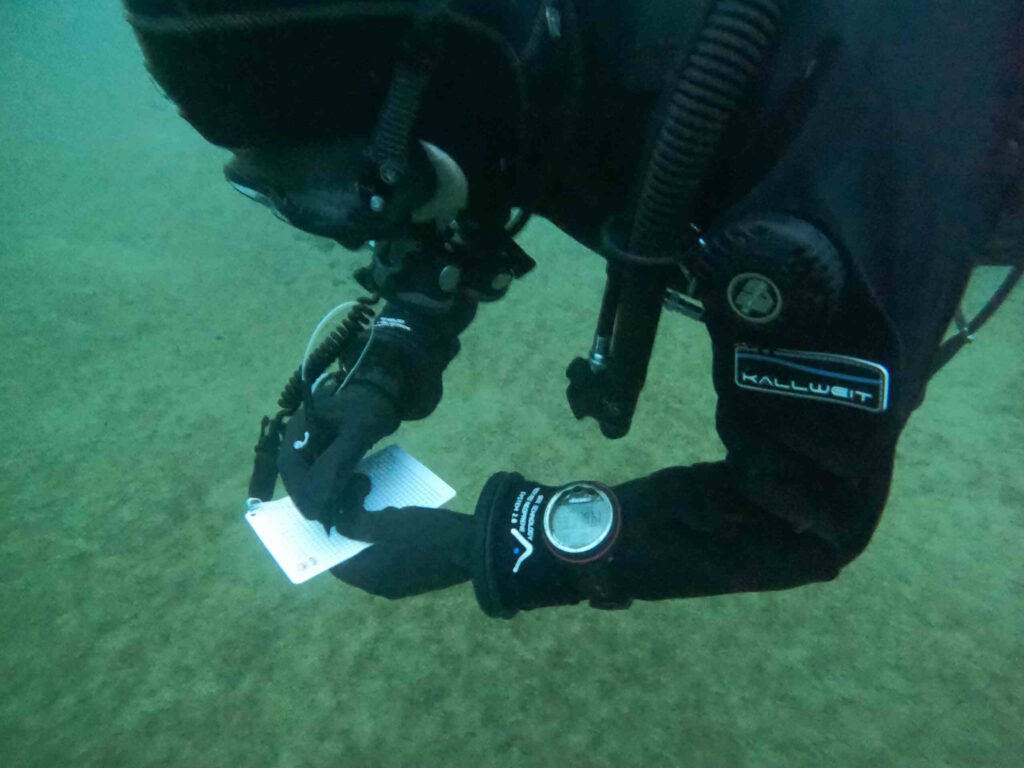 Gerätetaucher unter Wasser schreibt etwas während des Tauchgangs auf seine Wetnodes.