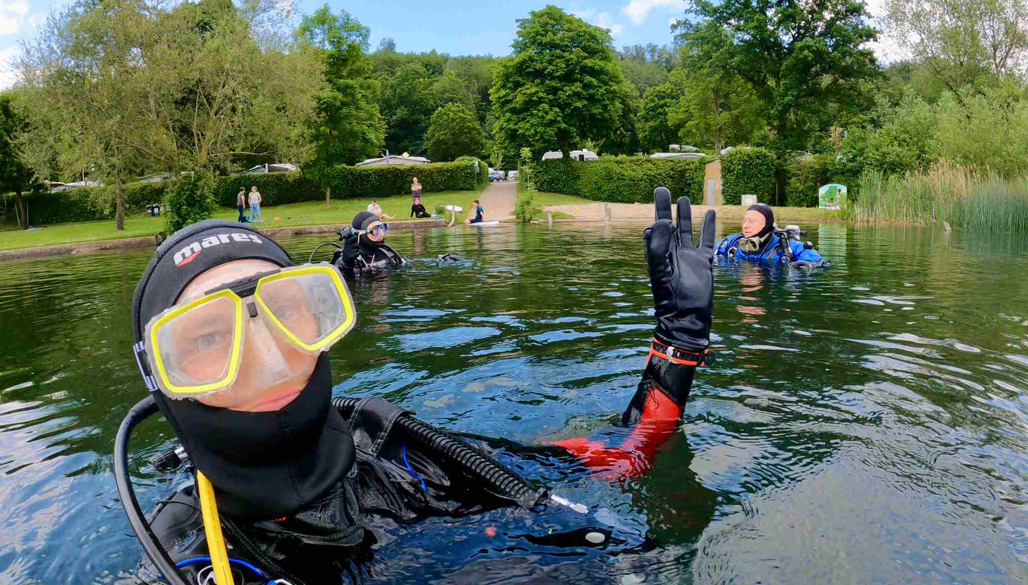 Bild mehrerer Taucher beim Abtauchen. Im Hintergrund der Strand vom Laacher See.