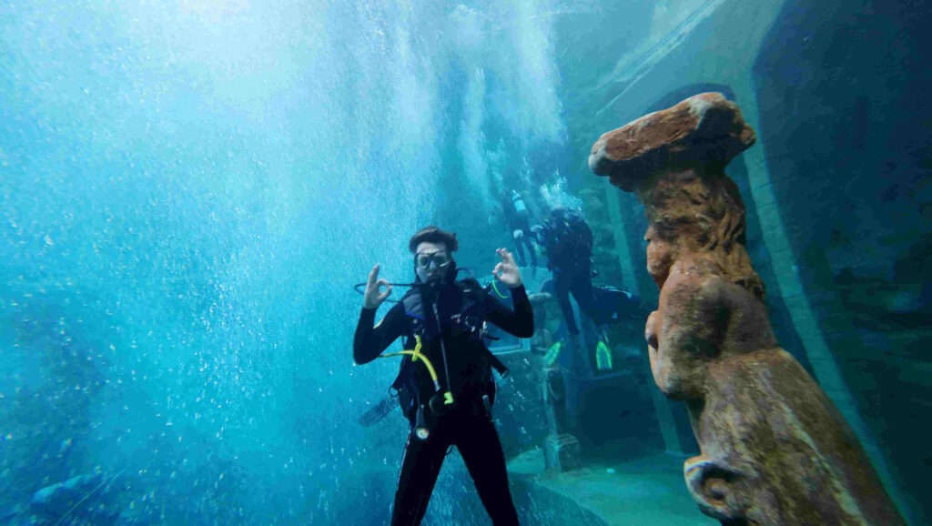 Fröhlicher Taucher unter Wasser mit vielen Luftblasen im Hintergund.